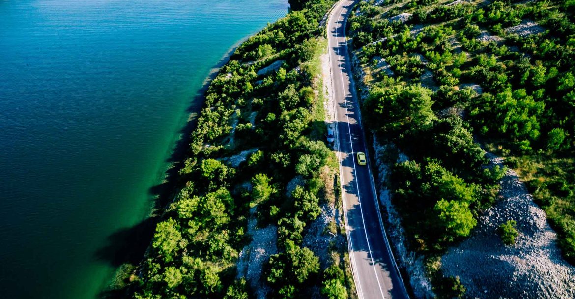 aerial-view-of-road-near-blue-sea-and-green-mounta-SPVWKR9