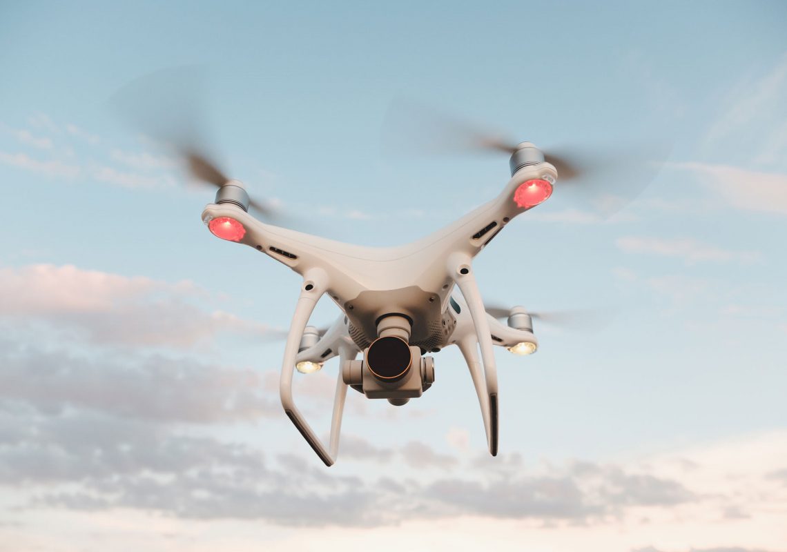 white-drone-hovering-in-a-bright-blue-sky-PMFRLG7
