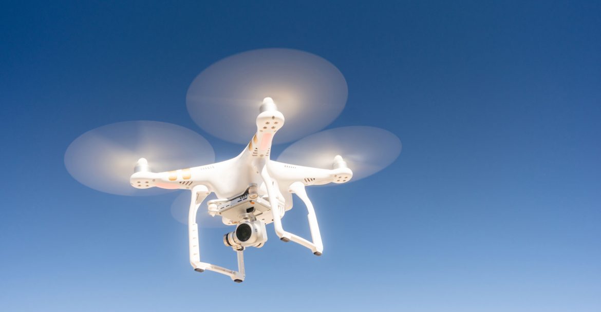 white-quadcopter-drone-flying-hoovering-blue-sky-PNJ53BD