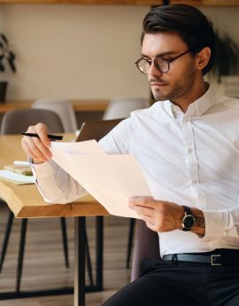 Young serious businessman in eyeglasses thoughtfully working with papers in modern office