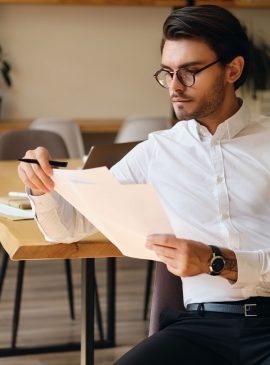 Young serious businessman in eyeglasses thoughtfully working with papers in modern office